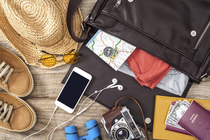 inpaklijst vakantie tas met telefoon, oortjes, paspoort, camera, comfortabele schoenen, zonnebril, hoofddeksel en landkaart.